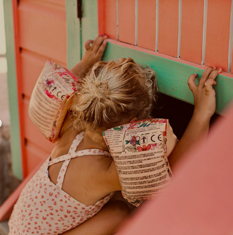 Criança loira de costas com boias salva-vidas cor-de-rosa em estrutura de madeira colorida