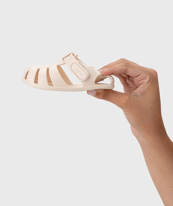 Sandália infantil bege com tiras e fecho de velcro segurada por mão