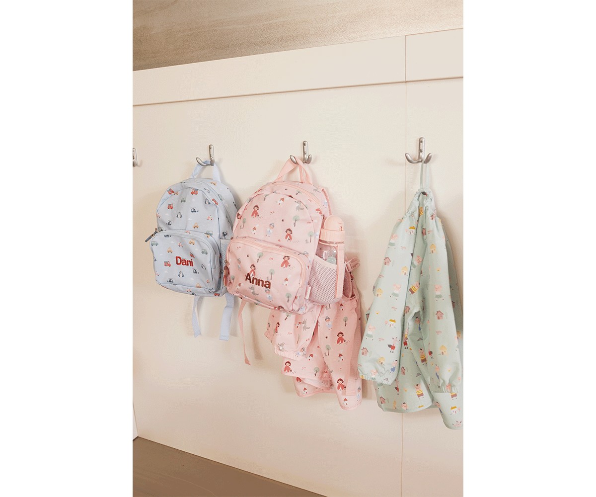 Mochilas azul e rosa com nomes e casaco azul pendurados numa parede