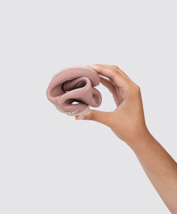 Mão segurando sapato feminino rosa flexível dobrado em espiral sobre fundo cinzento