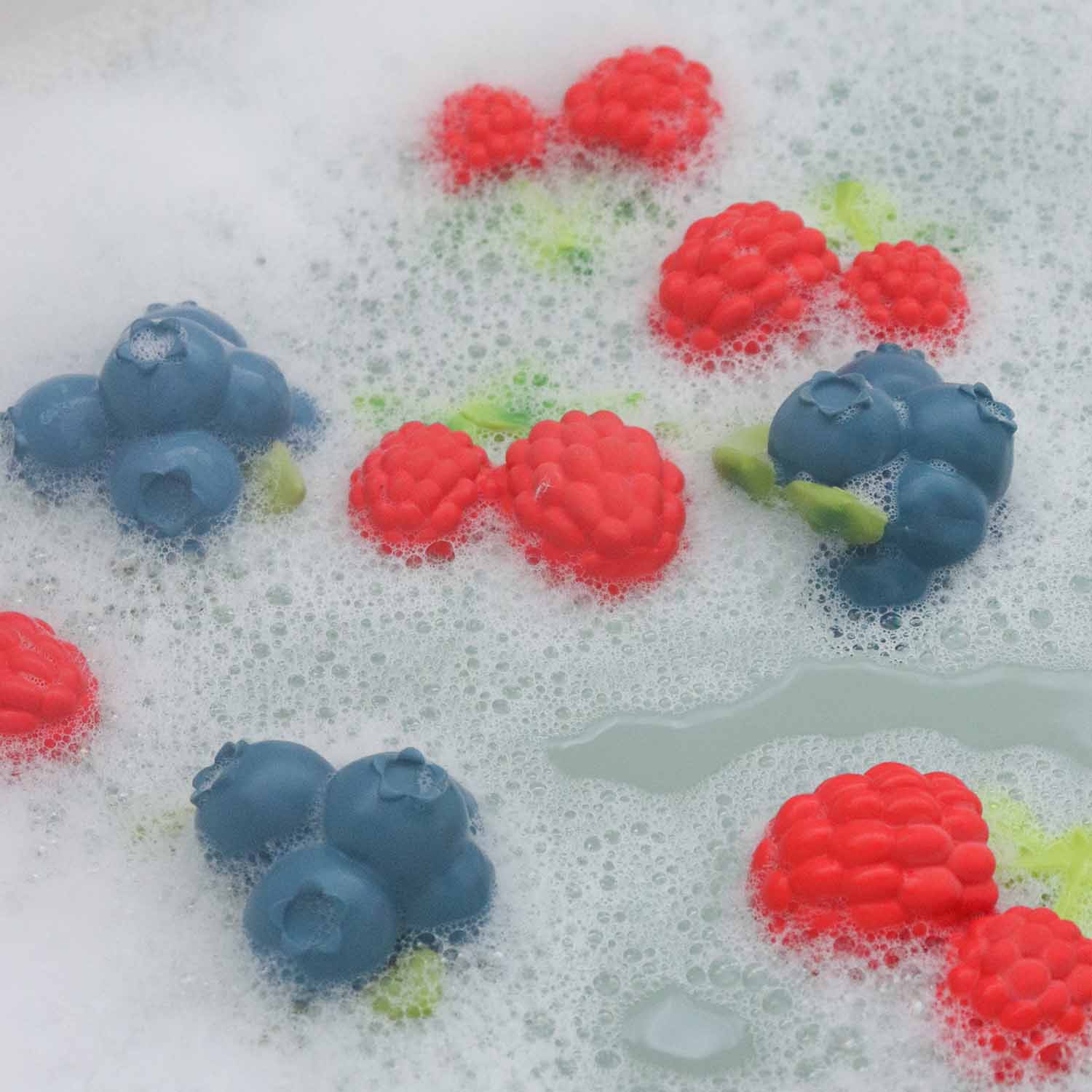 Sabonetes em forma de frutas vermelhas e mirtilos azuis na espuma branca