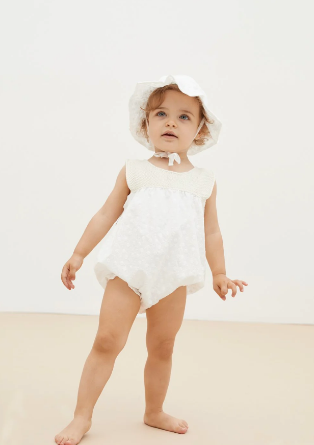Bebé com macacão branco e chapéu branco de tecido leve
