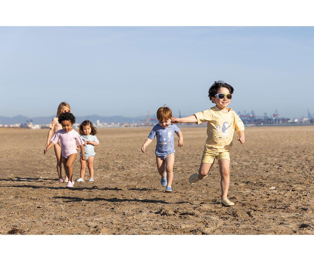 Crianças a correr na praia com roupas de verão coloridas em tons pastel