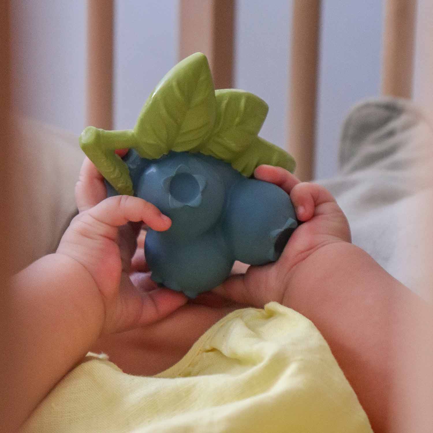 Boneco de bebé emborrachado azul e verde segurado por mãos pequenas em berço de madeira.