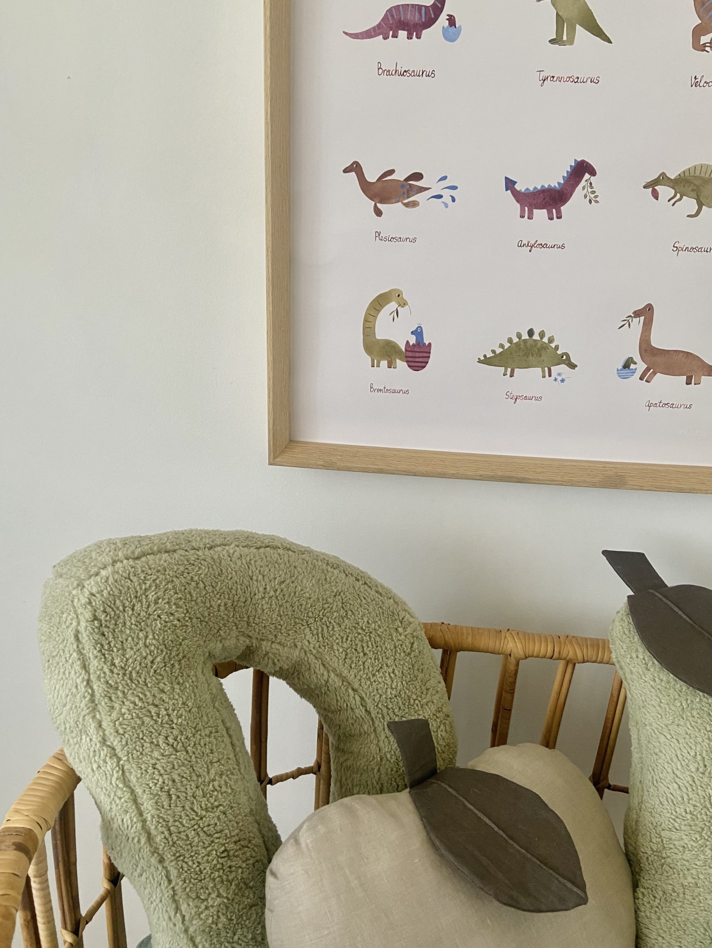 Almofadas verdes e bege em cadeira de madeira com poster de dinossauros na parede