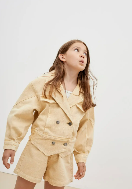 Criança com casaco e calções beges com botões pretos em fundo branco