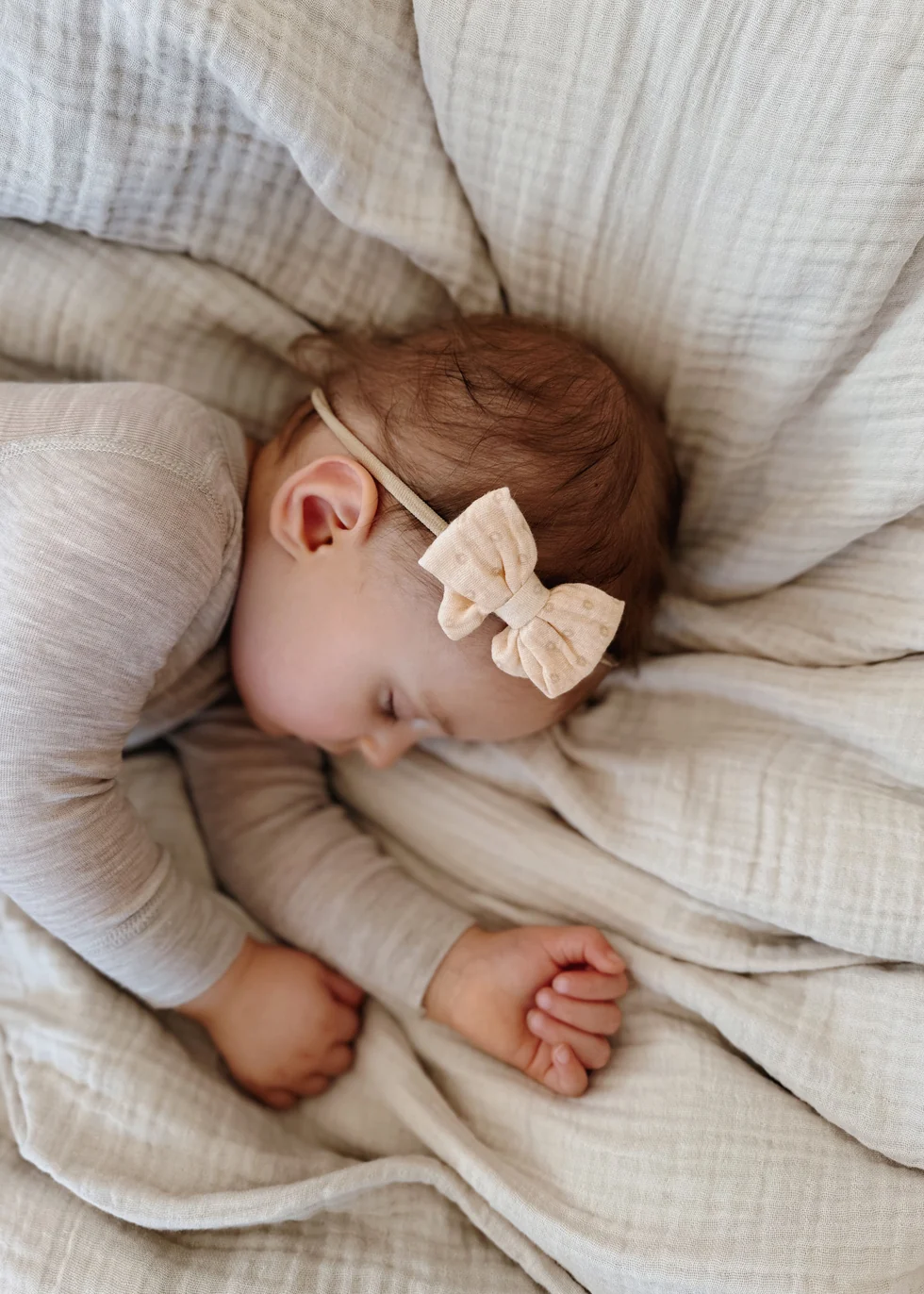 Bebé deitado com roupa bege e fita de cabelo com laço