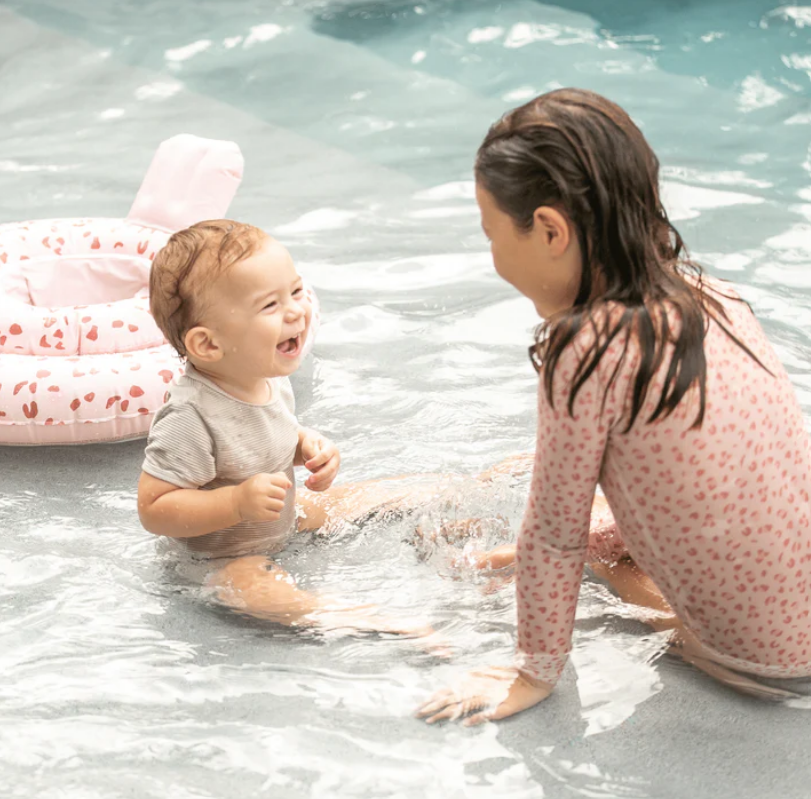 Bebé e criança na água com roupas de banho cor-de-rosa e cinzento e insuflável rosa