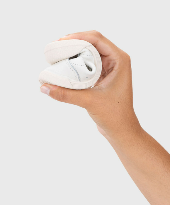 Sapato branco flexível dobrado na mão num fundo cinzento claro