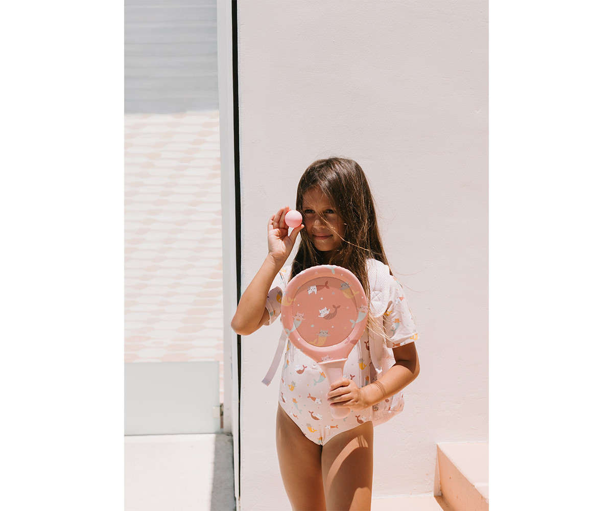 Menina com fato de banho e raquete de jogo de praia rosa com desenhos segurando uma bola rosa