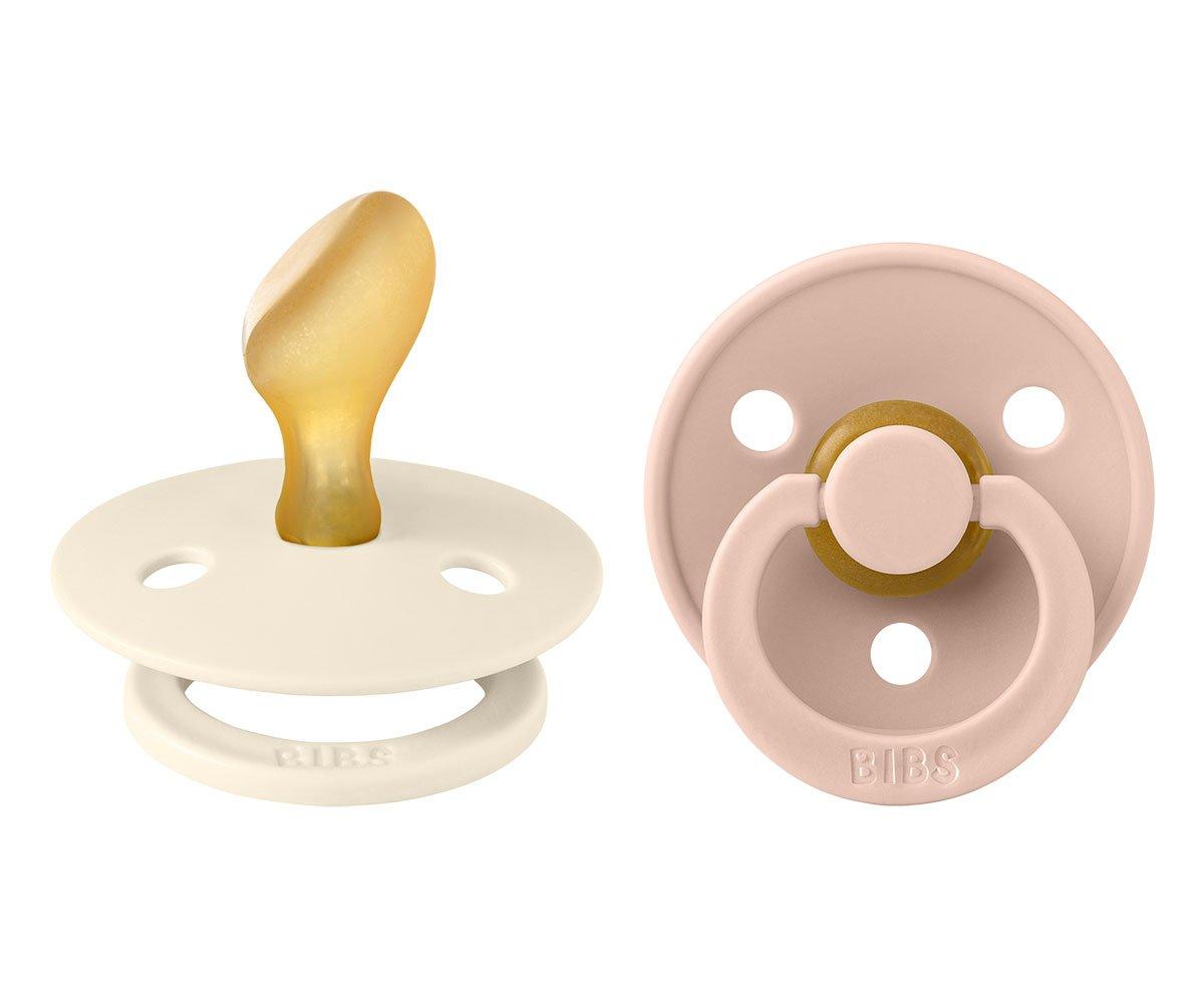 Duas chupetas BIBS, uma branca com tetina âmbar, outra rosa clara com anel.