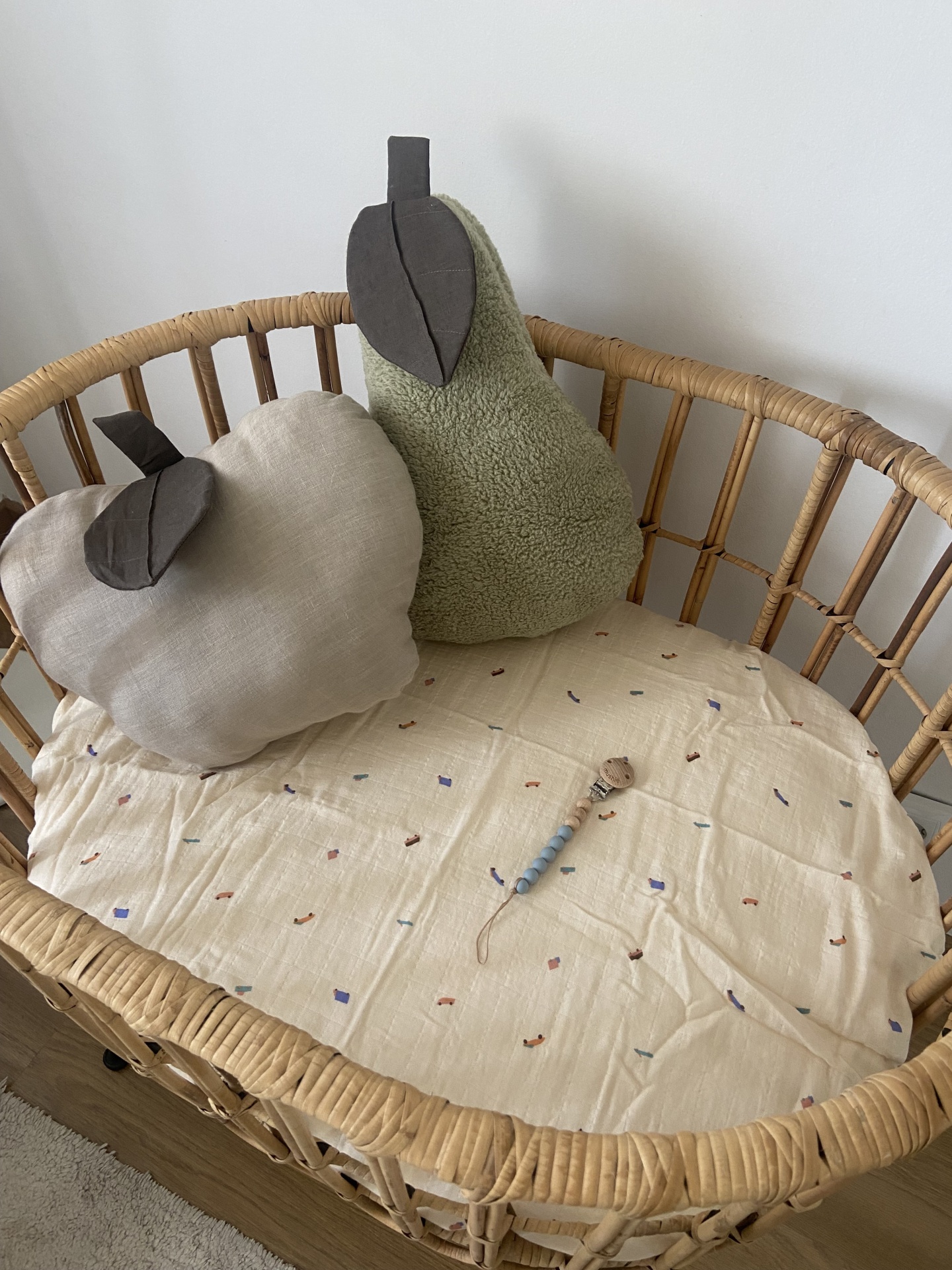 Berço de verga com almofadas em forma de frutas e chocalho em colchão estampado