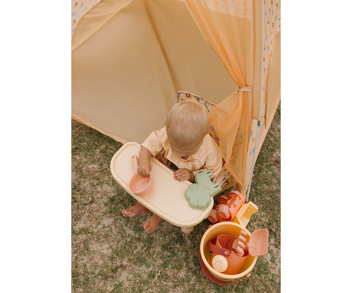 Bebé sentado em cadeira com brinquedos e tenda amarela no exterior
