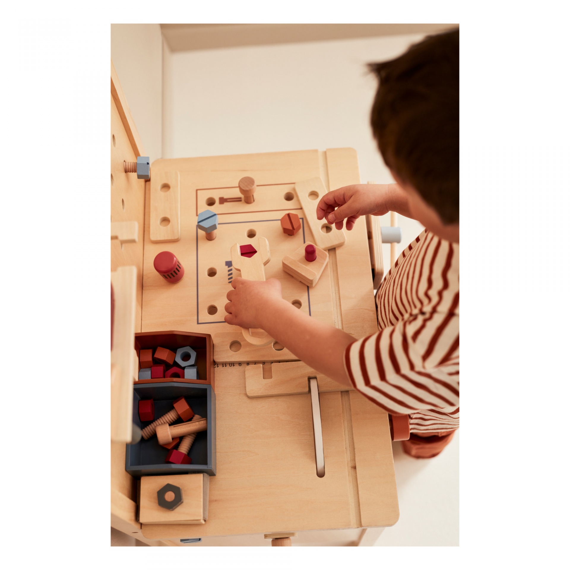 Criança a brincar numa bancada de brinquedo em madeira com peças coloridas e parafusos
