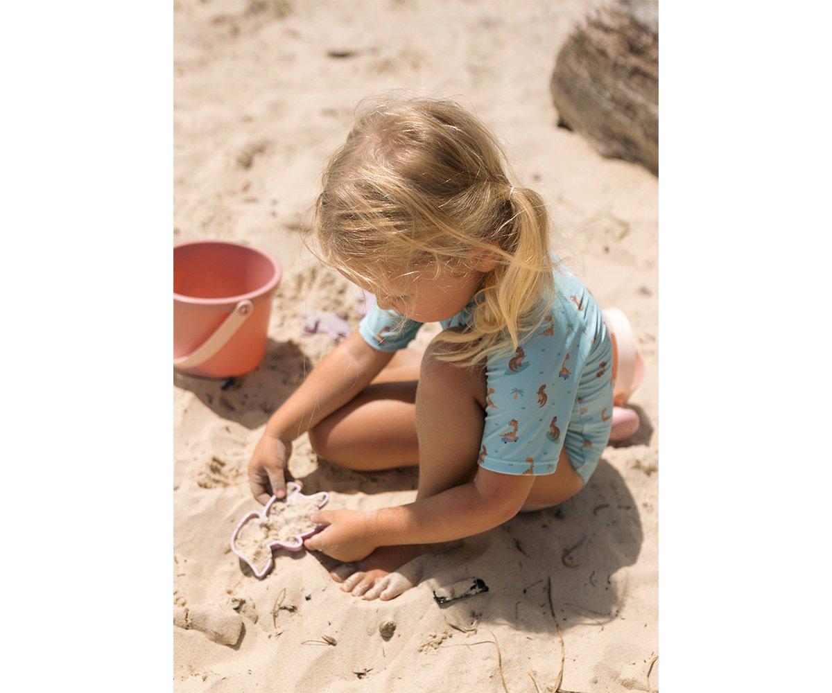 Criança na praia a brincar na areia com moldes e balde