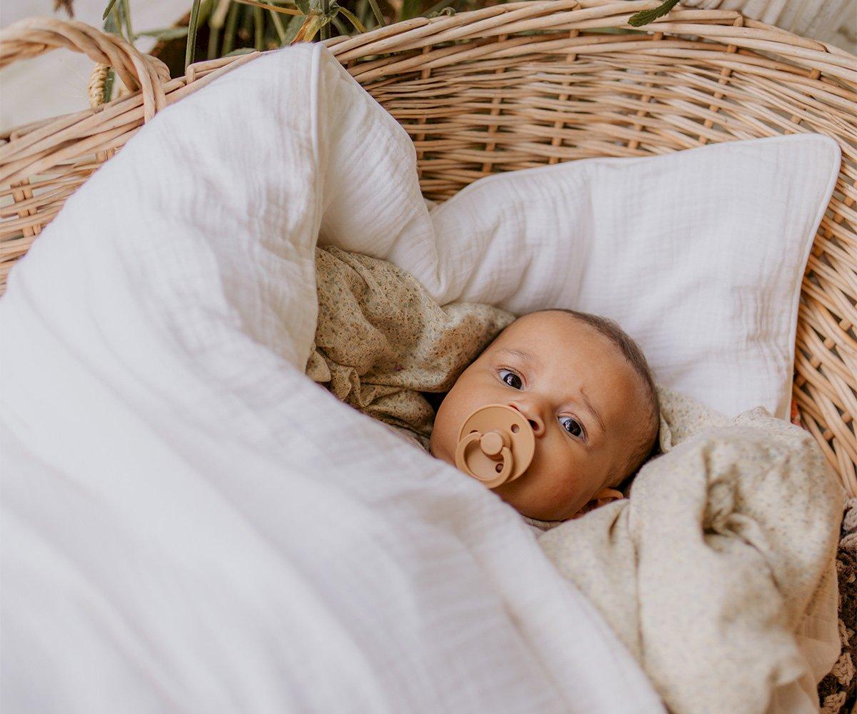 Bebé com chupeta numa cesta com mantas brancas e bege