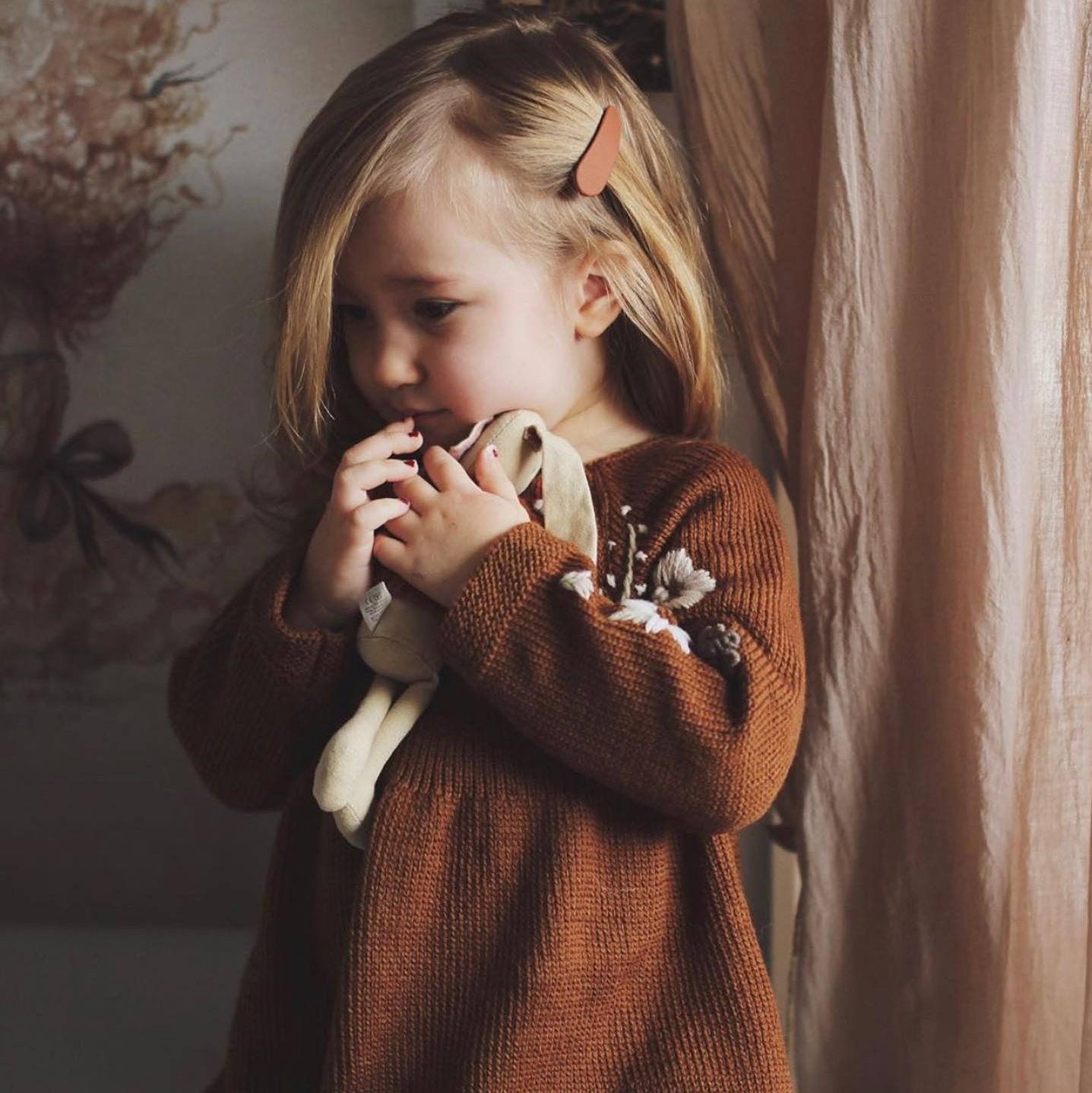 Menina com vestido de malha castanho segurando boneco de pano