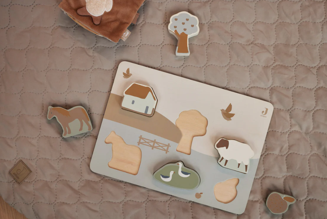 Tabuleiro de encaixe de madeira com peças decorativas sobre um edredão cinza com padrão de nuvens
