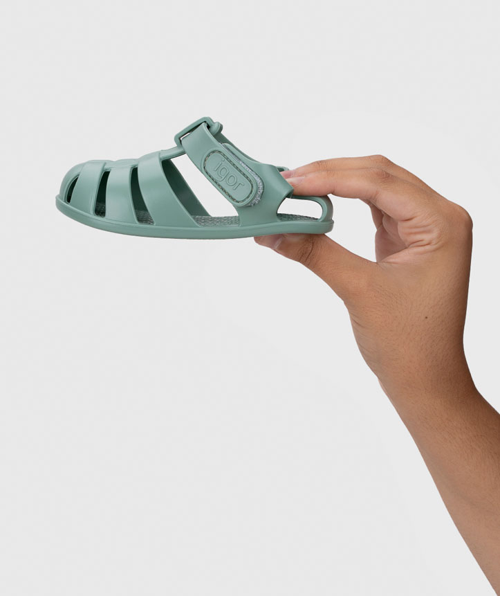 Sandália verde de plástico para crianças com fecho ajustável sendo segurada por uma mão
