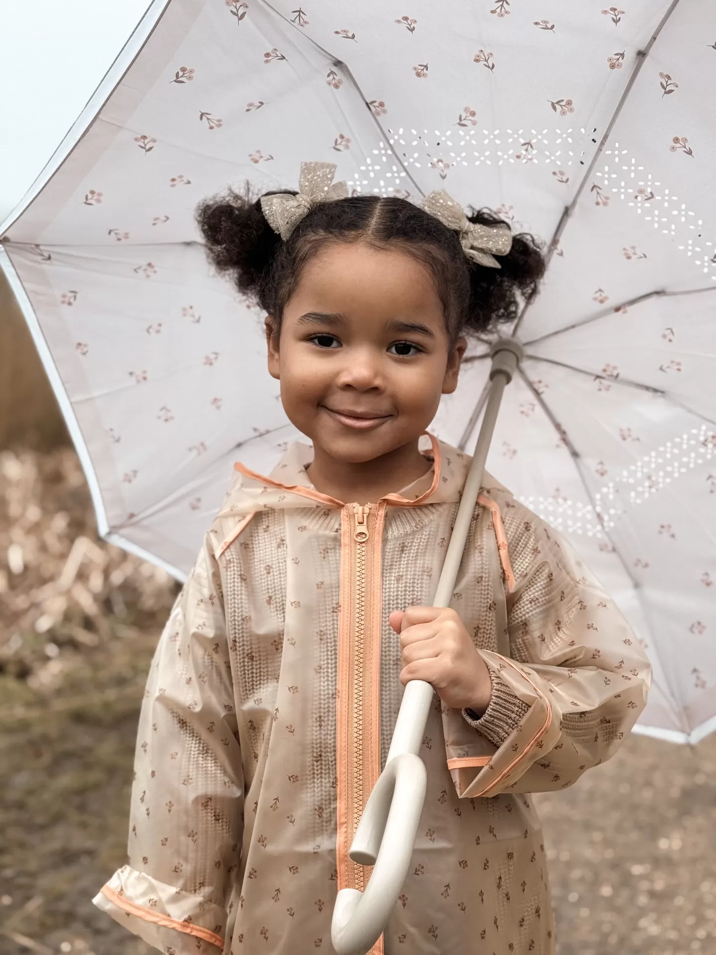 Criança com casaco impermeável bege e guarda-chuva branco floral ao ar livre