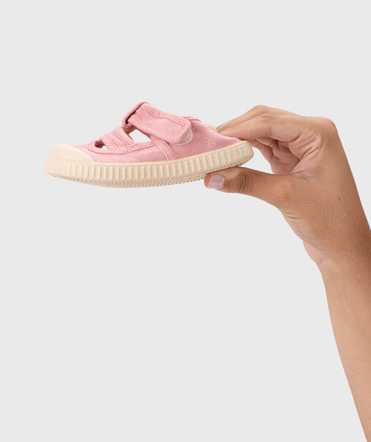 Tênis infantil rosa com sola creme e fechos de velcro, segurado por uma mão.