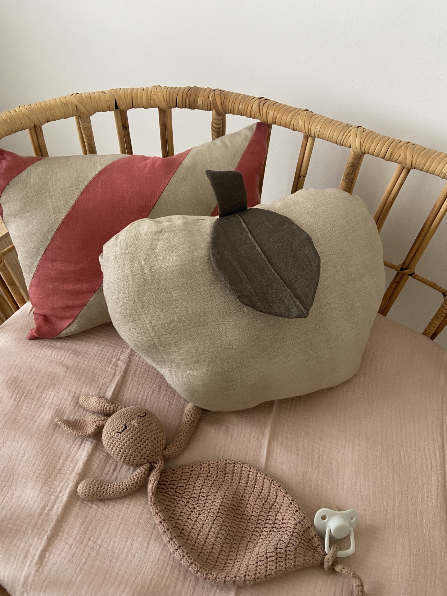 Almofadas em tecido e brinquedos sobre cama de rattan com cobertor rosa