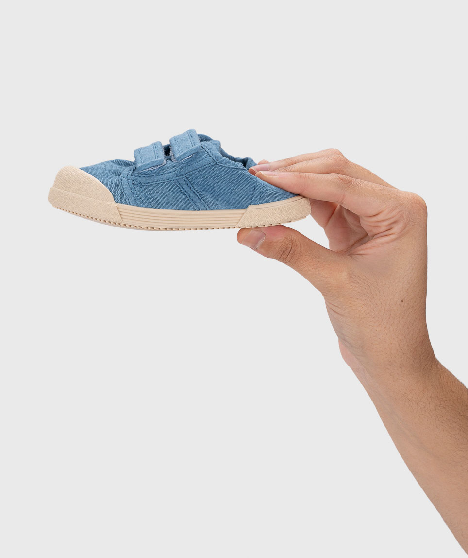 Sapato infantil azul de tecido com sola e biqueira bege segurado por uma mão