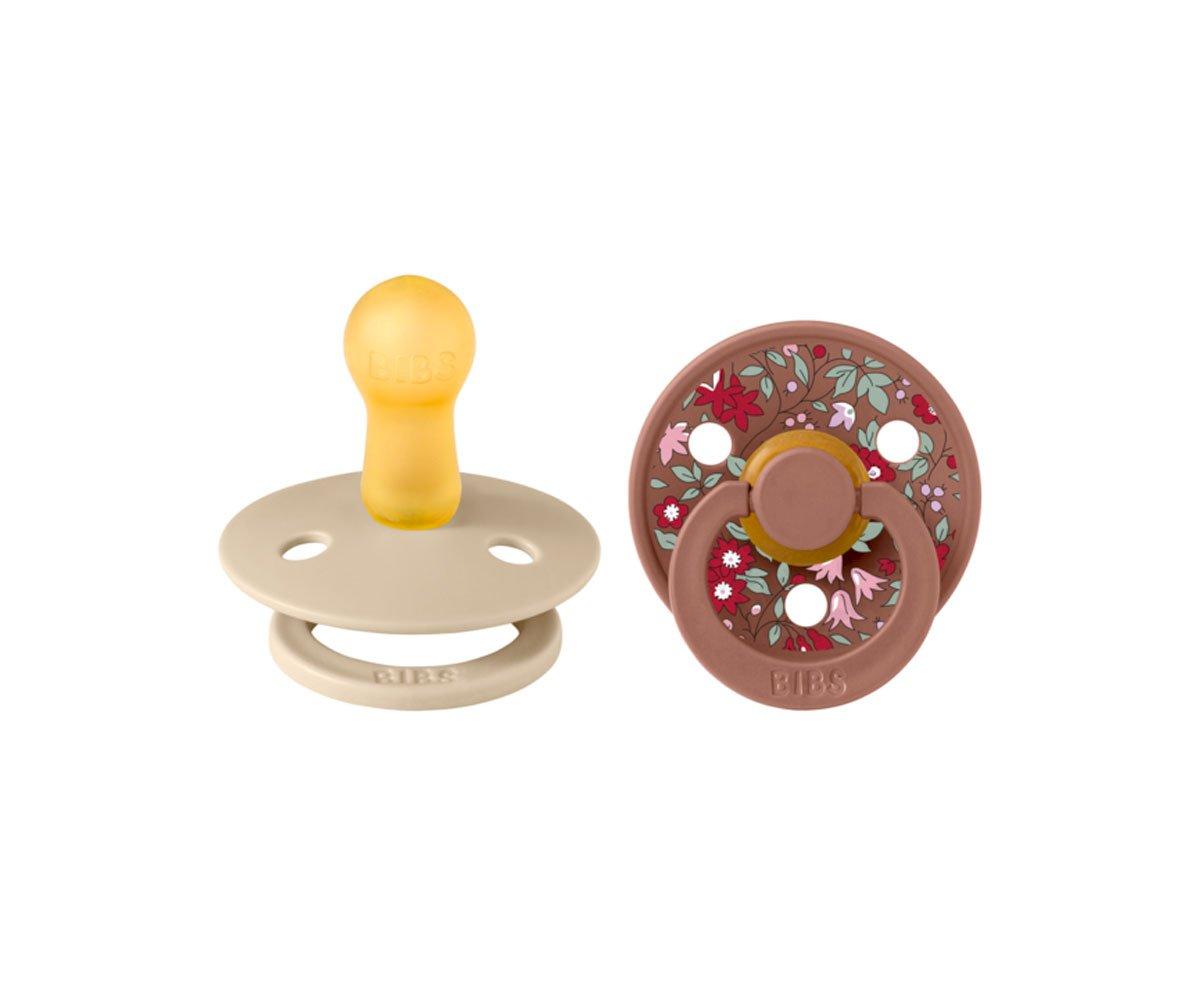 Dois chupetas BIBS, uma amarela e beige, outra floral castanha.