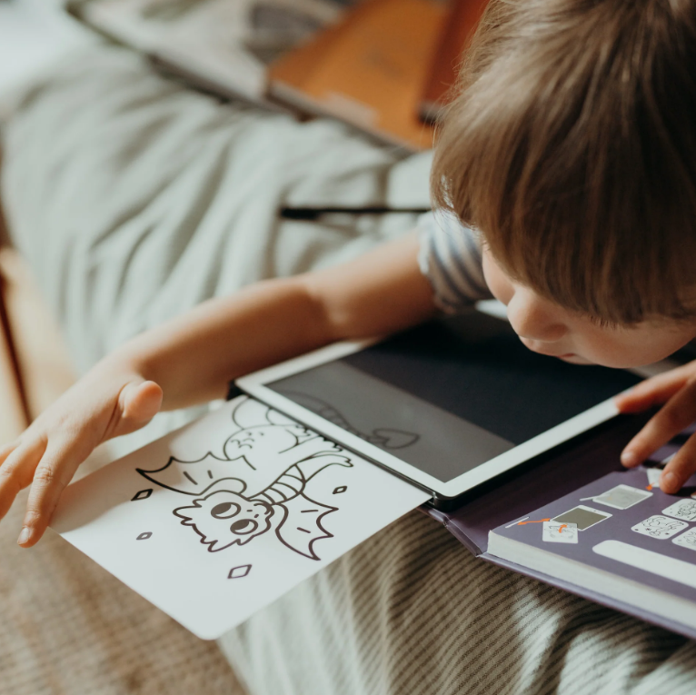Criança retirando desenho de dragão de um tablet na cama