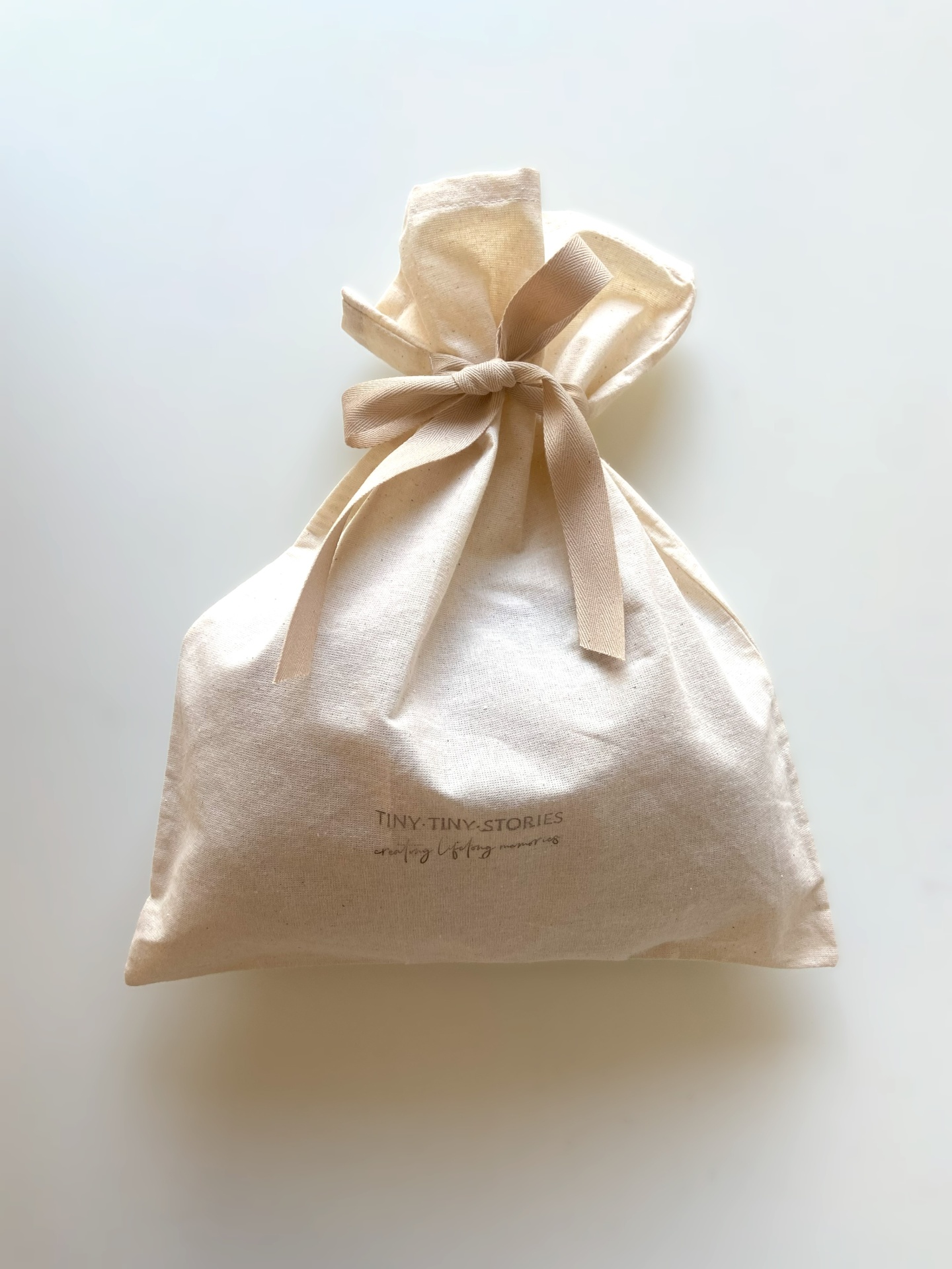 Saco de tecido beige com laço e texto TINY TINY STORIES