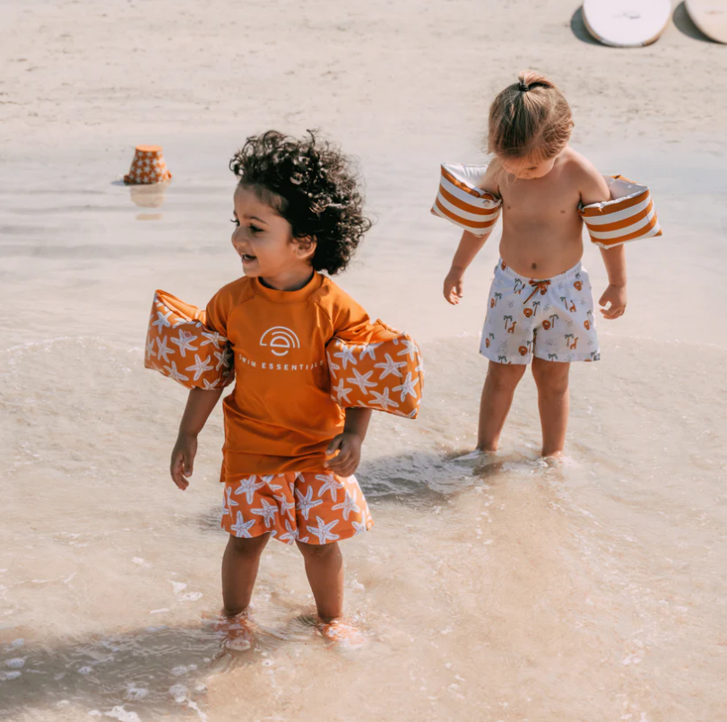 Duas crianças com fatos de banho e equipamentos de segurança na água rasa da praia