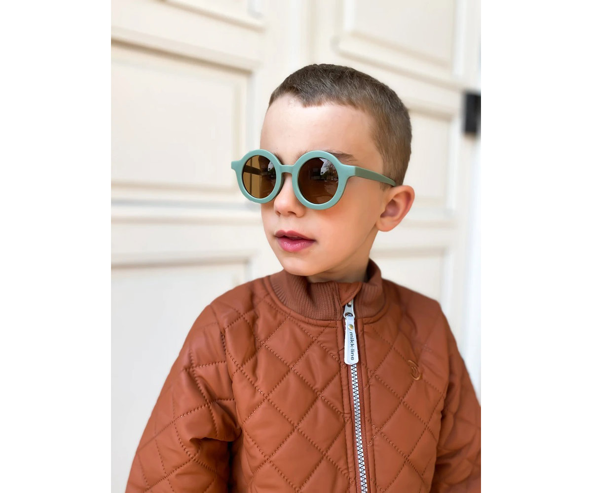 Criança com óculos de sol verdes e casaco castanho acolchoado