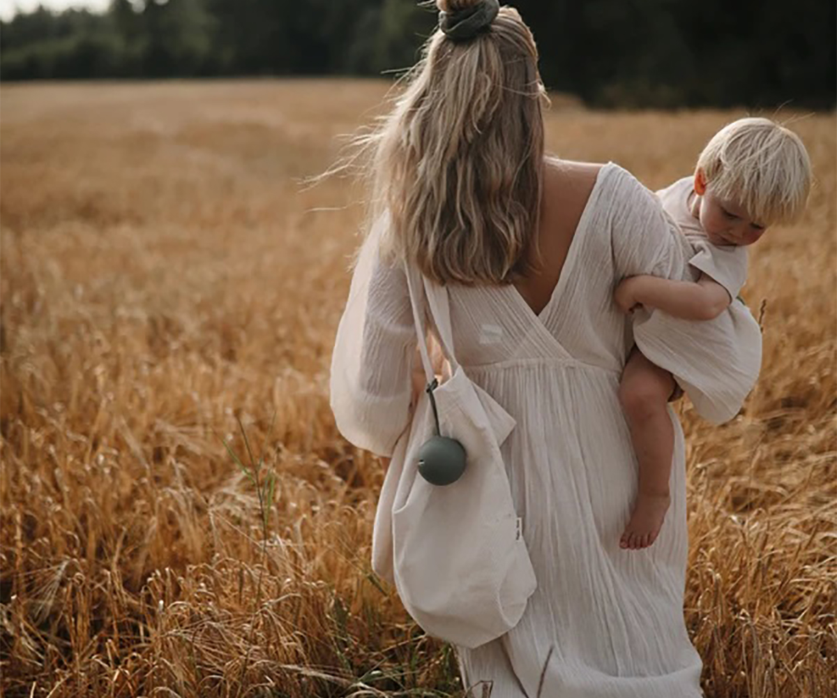 Mulher de costas com vestido branco a segurar criança num campo de trigo.