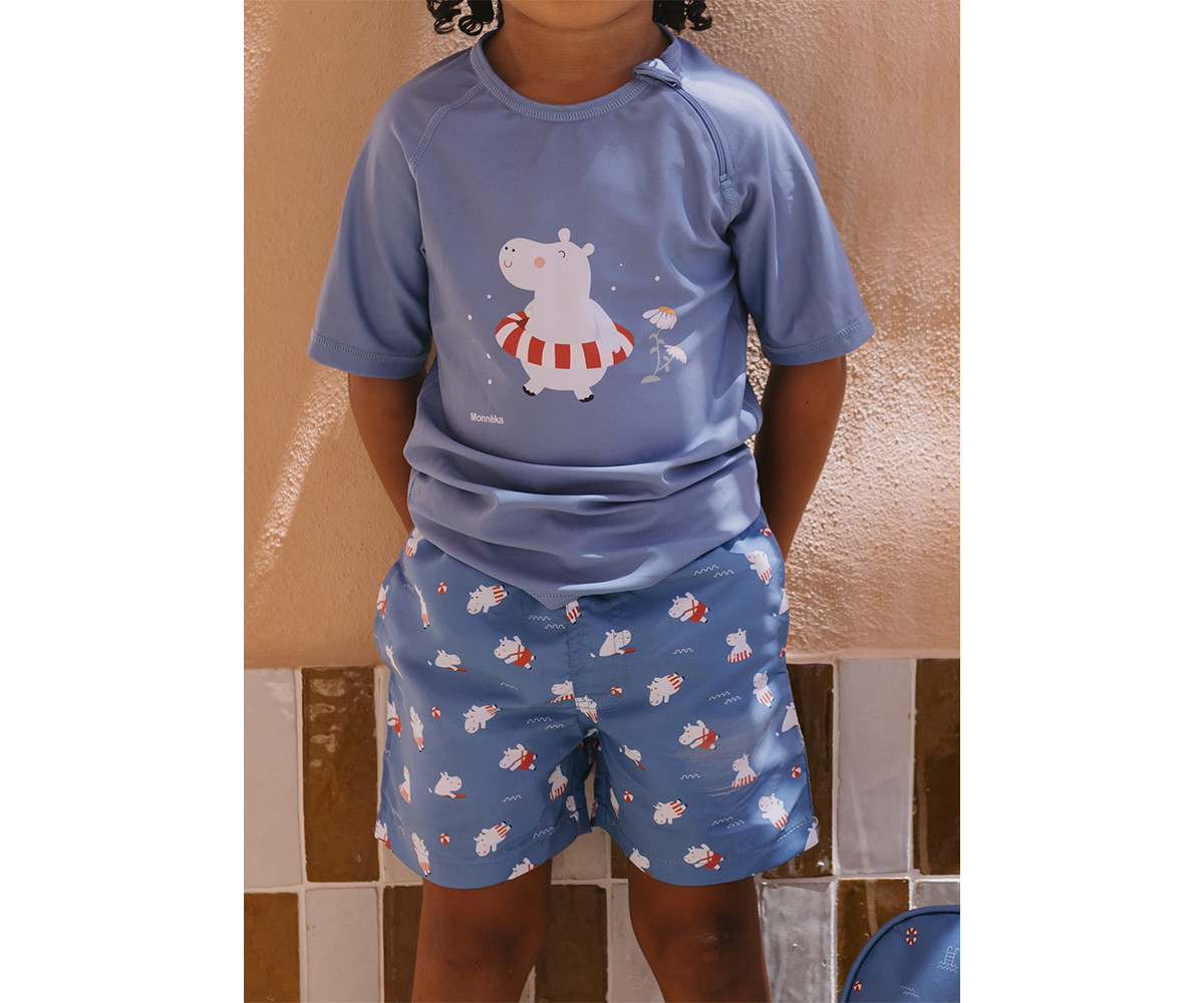 Roupa infantil azul com hipopótamos e padrões, criança em fundo neutro.