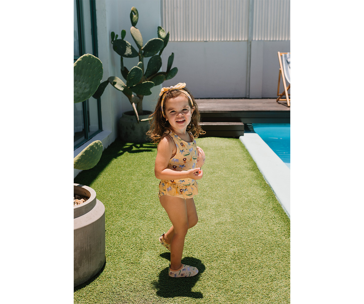 Menina com fato de banho amarelo com padrão de animais junto a piscina