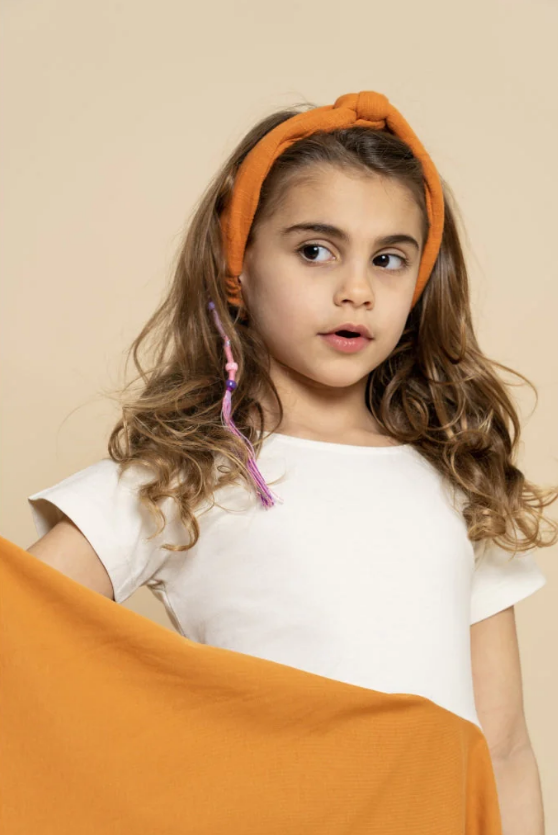 Menina com faixa de cabelo laranja, t-shirt branca e tecido laranja