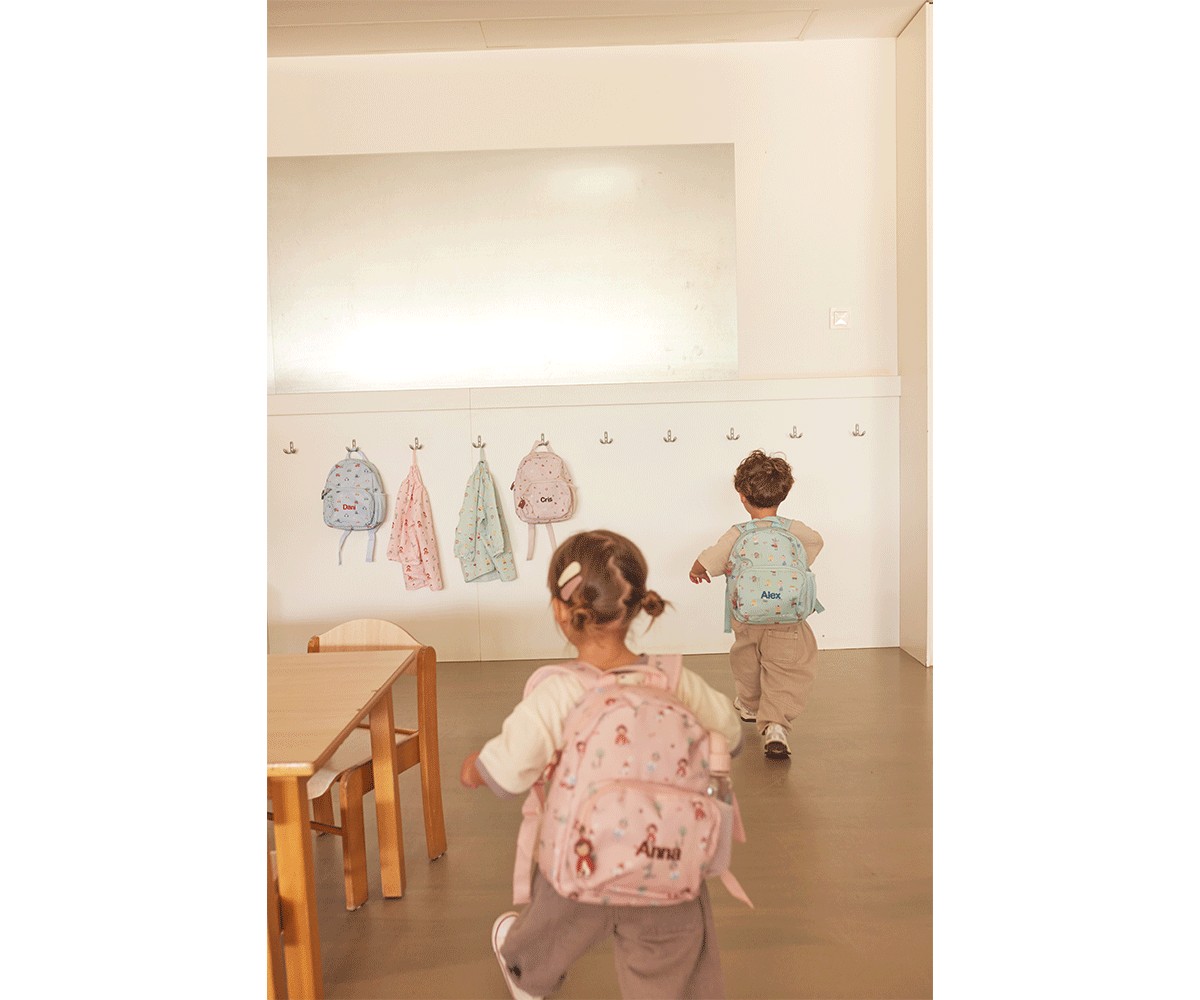 Crianças com mochilas coloridas em ambiente interior com mochilas penduradas na parede