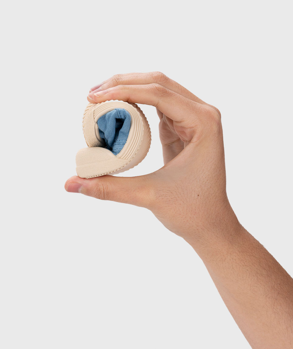 Mão segurando sapato infantil dobrado com sola bege e tecido azul