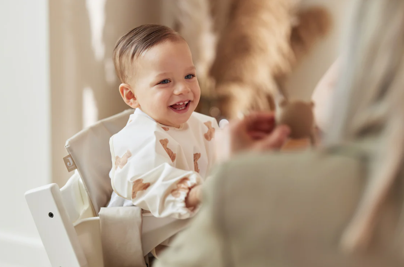 Cadeira alta branca com bebé sorridente e camisa branca com padrão bege