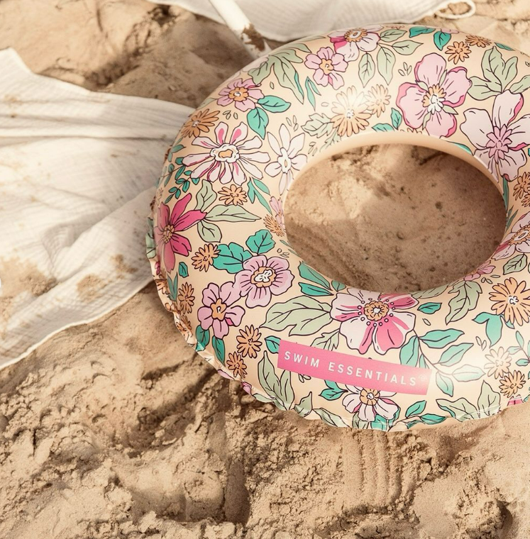 Bóia de piscina floral sobre areia perto de toalha branca