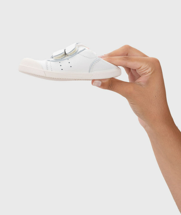 Sapato branco de criança com velcro segurado por mão