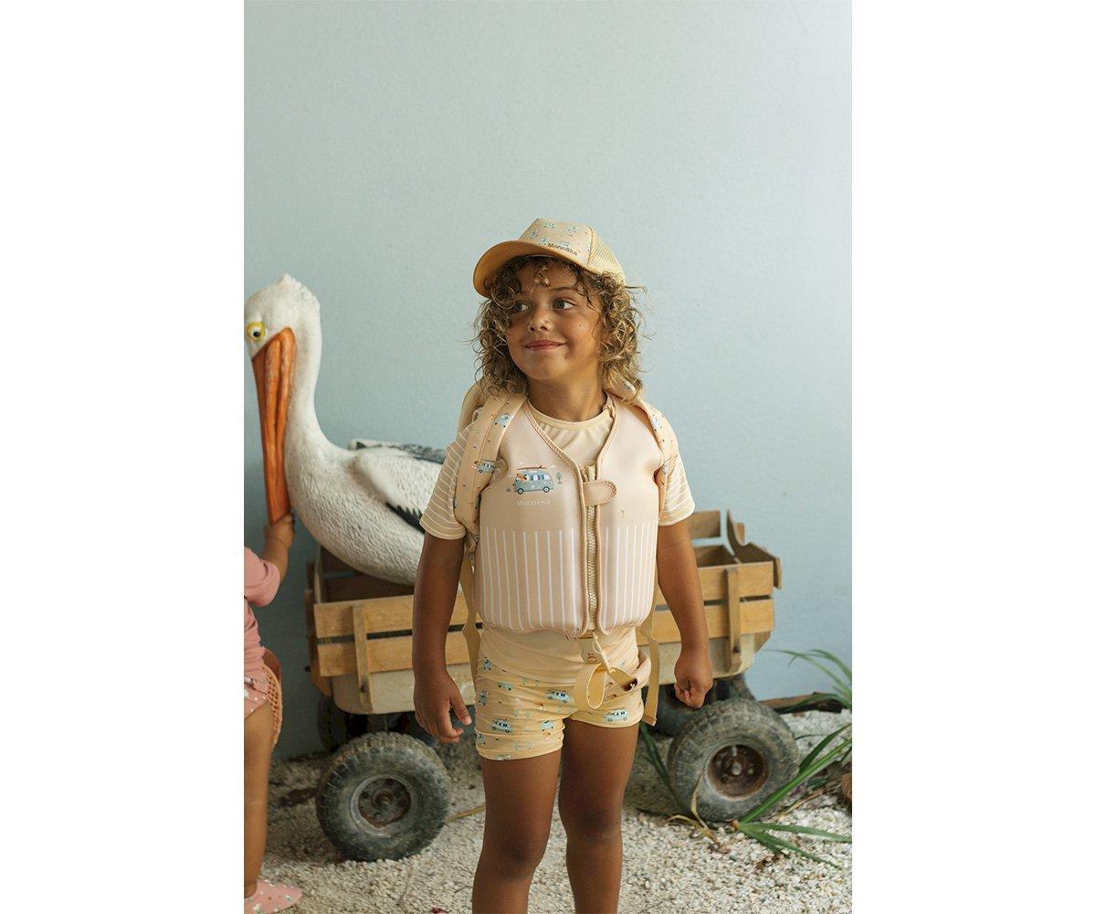 Criança com colete salva-vidas e boné em ambiente com carrinho de madeira