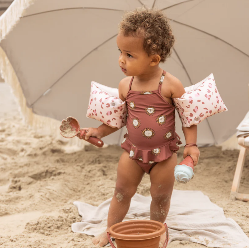 Criança com fato de banho castanho e mangas infláveis na praia