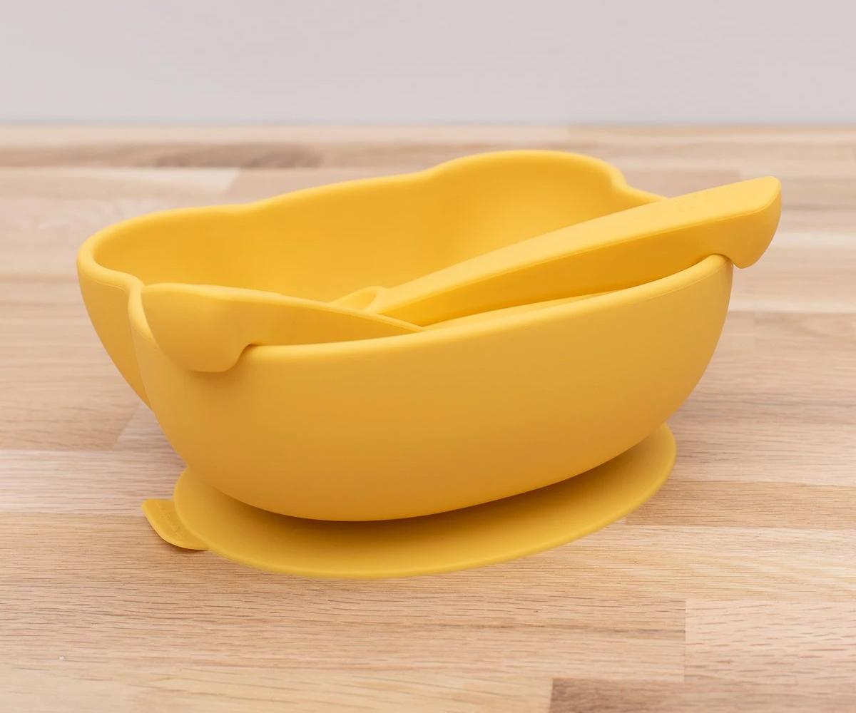 Taça amarela de silicone com espátula numa mesa de madeira