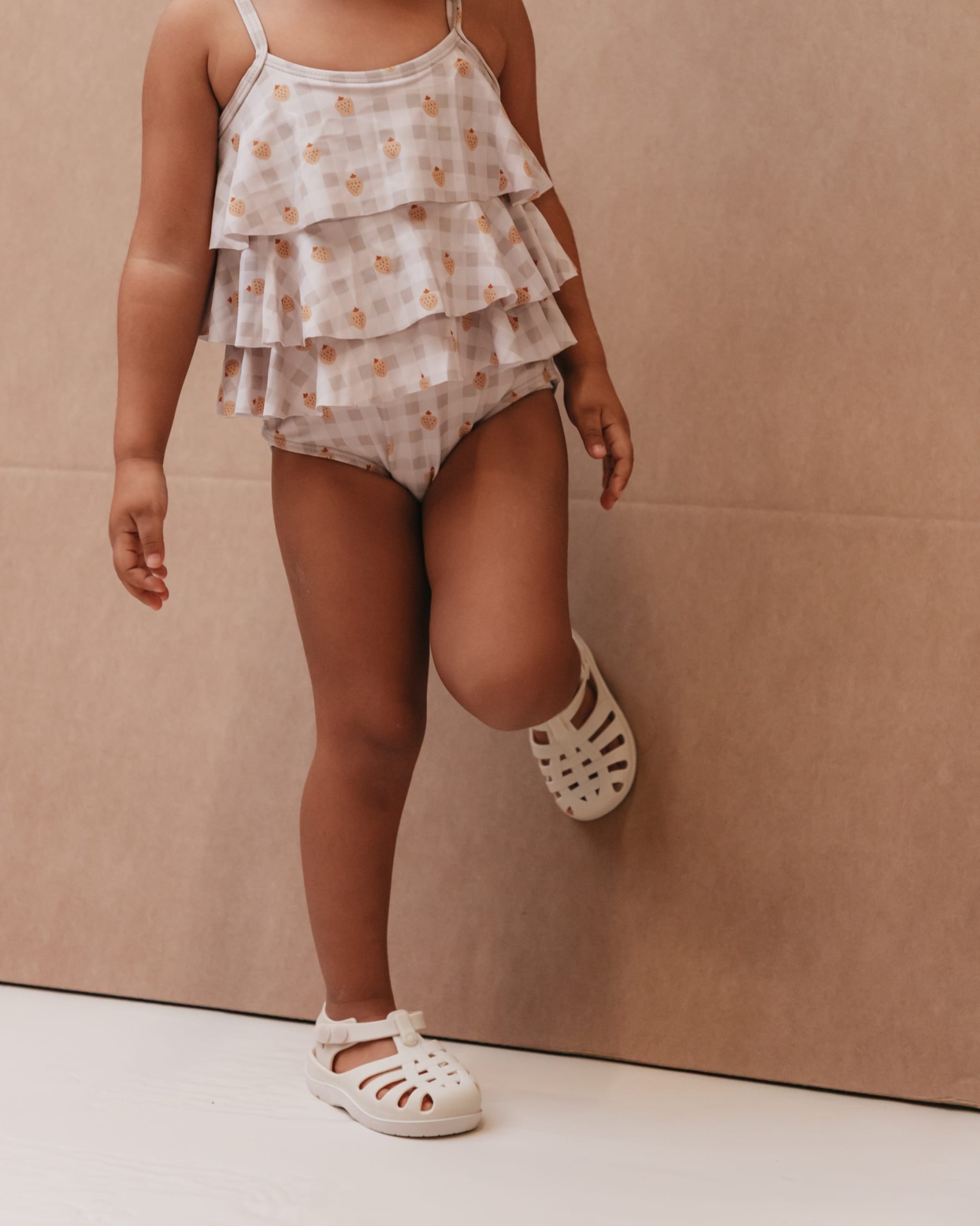 Fato de banho para criança com folhos e sapatos brancos.