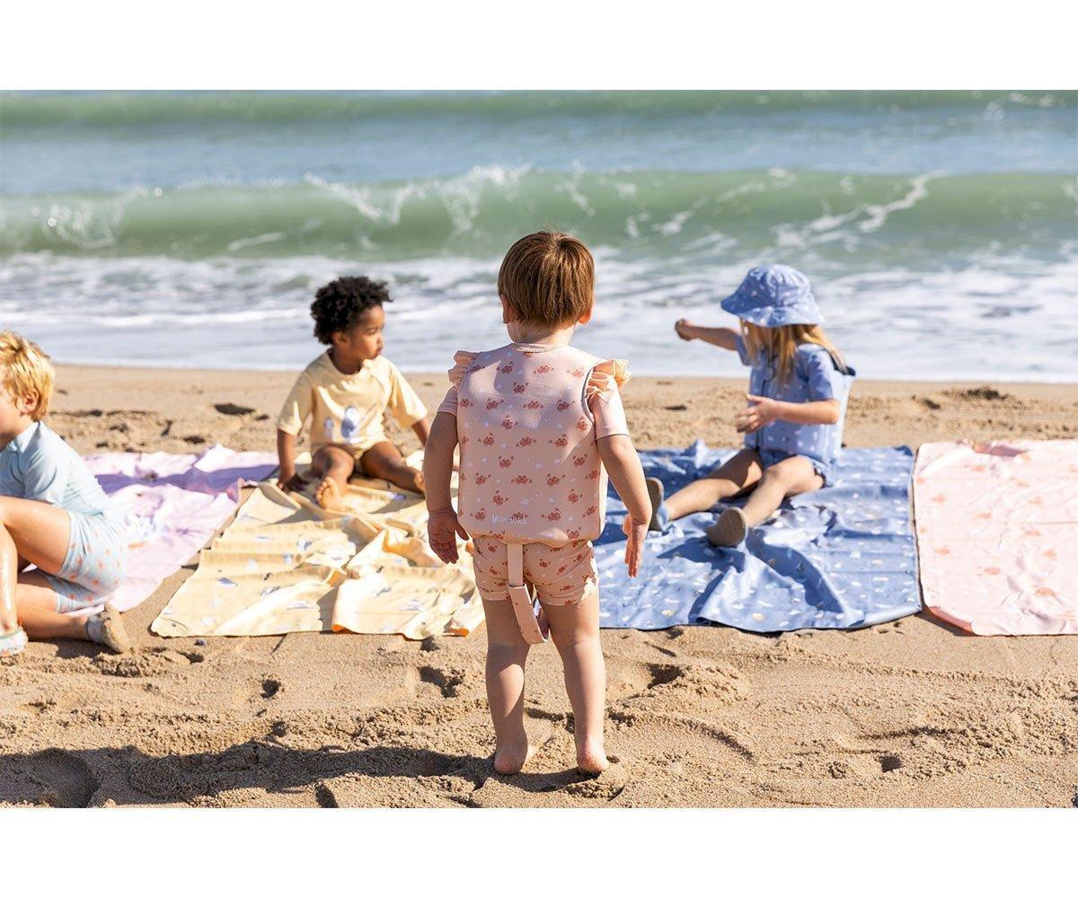 Crianças brincam na praia junto a toalhas coloridas na areia