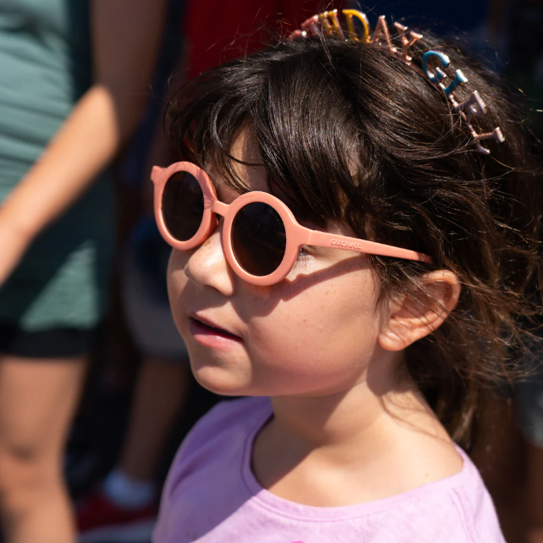 Criança com óculos de sol cor-de-rosa e tiara 'BIRTHDAY GIRL' em ambiente exterior