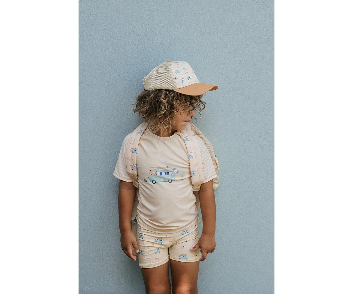 Criança a vestir roupa clara com padrões azuis e boné contra parede cinzenta