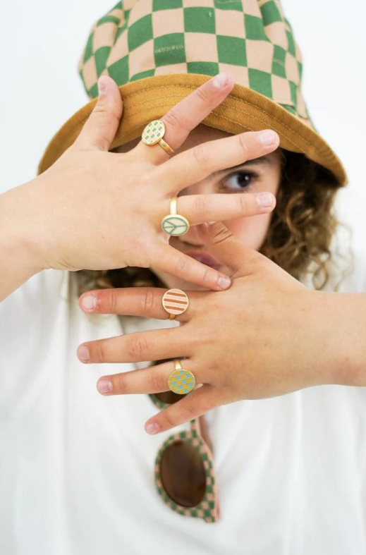 Pessoa com chapéu de xadrez verde e bege e anéis coloridos nas mãos