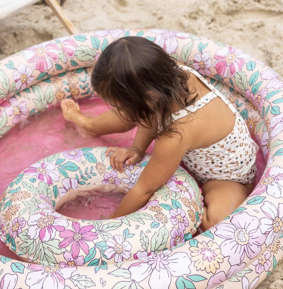 Menina numa piscina insuflável floral rosa na praia